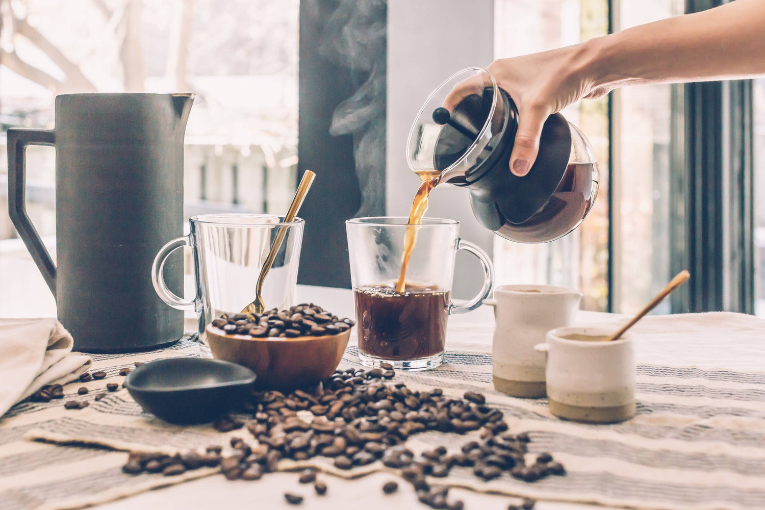 Pouring a fresh cup of coffee on a table with fresh roasted coffee beans spread around the table.
